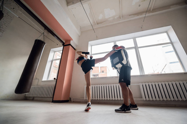 Młoda sportowiec w dobrej kondycji fizycznej prowadzi trening kickboxingu pod okiem doświadczonego trenera męskiego - Zdjęcie, obraz