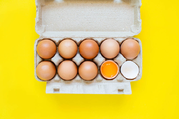 Closeup popraskané hnědé vejce a vejce v papírových krabicích umístěných bok po boku na žlutém pozadí. - Fotografie, Obrázek