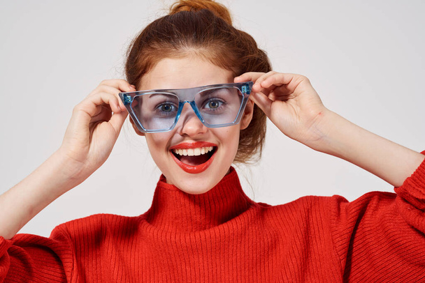 hermosa mujer en un suéter rojo con gafas azules sobre un fondo claro - Foto, Imagen