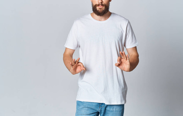 Ein Mann in weißem T-Shirt auf hellem Hintergrund gestikuliert mit den Händen abgeschnitten Blick auf Jeans Copy Space - Foto, Bild