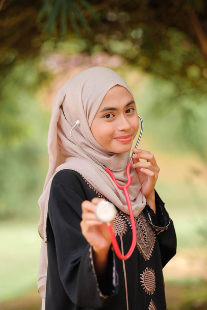 Giovane preda Asean medico femminile con hijab tenendo stetoscopio nel giardino dell'ospedale. Concetto di servizio medico e sanitario. - Foto, immagini