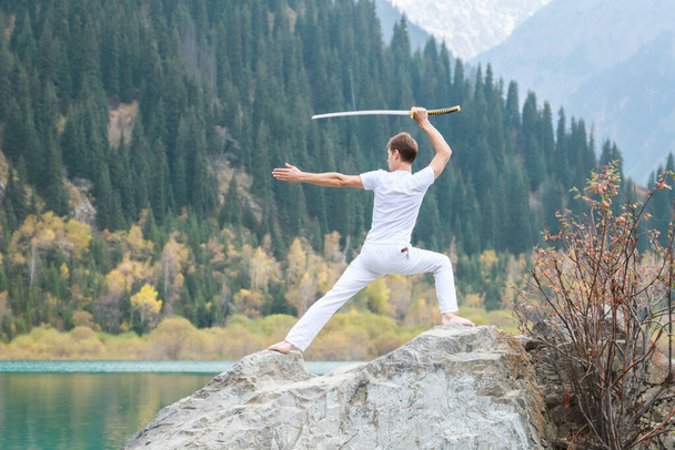 Un joven se levanta sobre una gran piedra y sostiene una espada japonesa en sus manos - Foto, Imagen