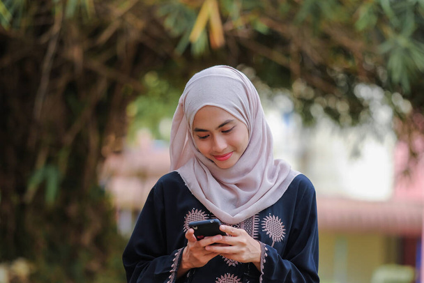 Portret pięknej muzułmanki noszącej hidżab za pomocą smartfonu.Technologia i koncepcja komunikacji. - Zdjęcie, obraz