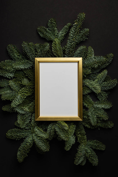 Empty golden border with garland of fir branches and cones on a black background. - 写真・画像