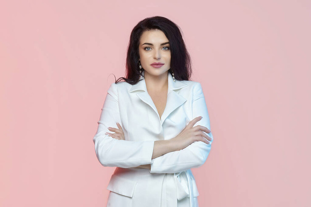 charming brunette with long hair and a white suit. photo shoot on a pink background - Photo, image