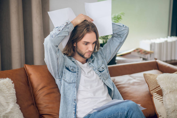 Young man in jeans shirt holding papers and looking stressed - Foto, Bild