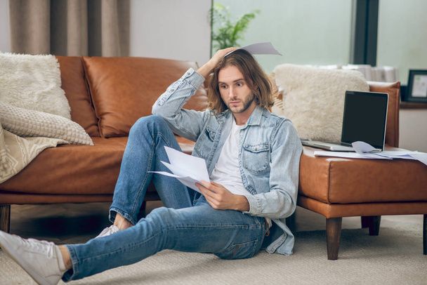 Young man in jeans shirt holding papers and looking stressed - Fotoğraf, Görsel