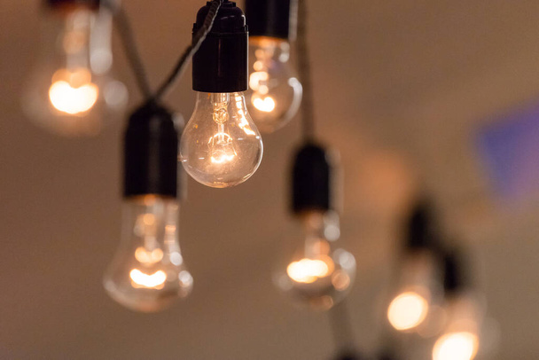 Close up view of vintage decorative light lamp bulb glowing on the ceiling indoors. Transparent lamps glowing with warm light. - Photo, Image