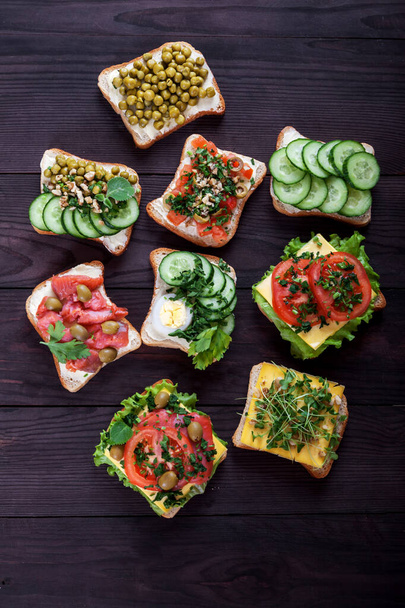 Toasts, sandwiches with cream cheese, cucumbers, tomatoes, salmon, sprouts, egg on a brown wooden background. Healthy food concept. Overhead - 写真・画像