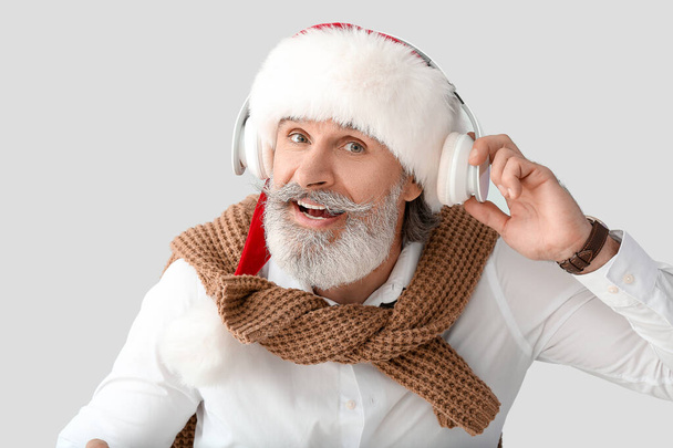 Senior man listening to Christmas music on grey background - Фото, изображение