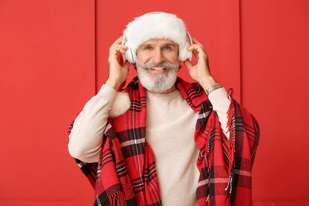 Senior man listening to Christmas music on color background - Photo, Image