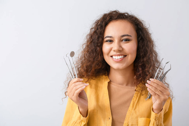 Beautiful young woman with dentist's tools on light background - Foto, Imagen