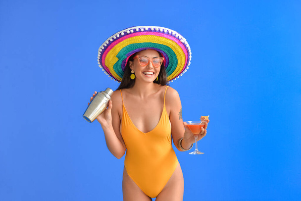 Gyönyörű fiatal nő fürdőruhában, sombrero kalap és koktél színes háttér - Fotó, kép