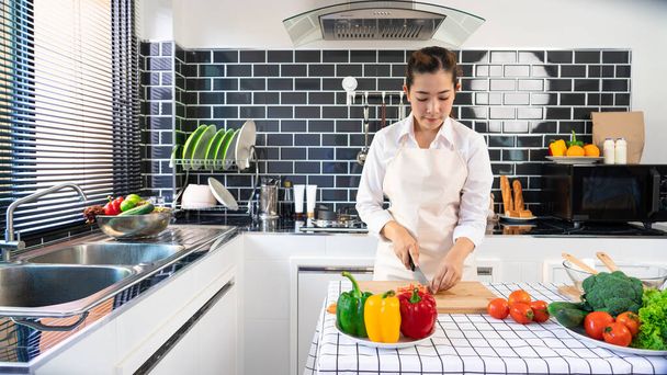young Asian woman is preparing healthy food vegetable salad by Cutting tomato for ingredients on cutting board on light kitchen, Cooking At Home and healthy food concept - Photo, Image