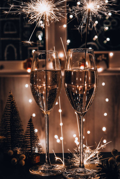 Deux verres de champagne mousseux au mousseux. Fond sombre avec bokeh clair jaune. Des jouets d'arbre de Noël sur la table. Feu du Nouvel An au bengale. Noël vacances d'hiver - Photo, image
