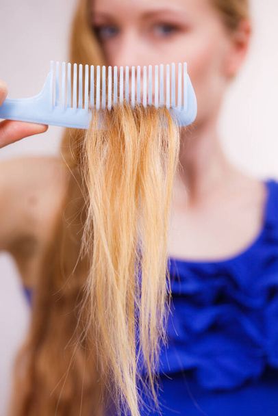 Haircare. Blonde girl showing her damaged dry hair ends on comb - Foto, immagini