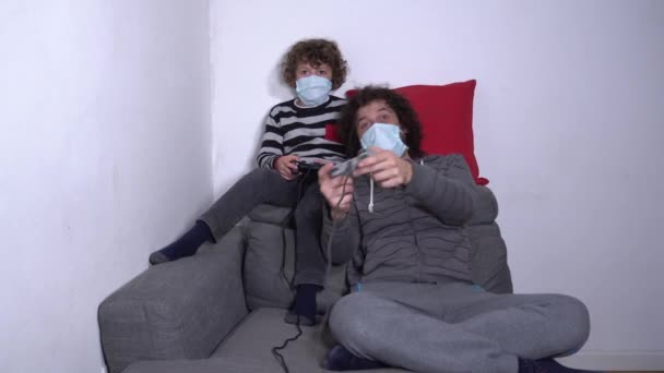 Evropa, Itálie, Milán - Otec a syn dítě chlapec 6 let sledování televize a hraní videoher s maskou během Covid-19 Coronavirus uzamčení karantény domů - Záběry, video