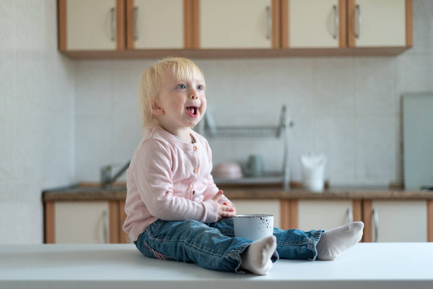 Portret van grappig blond kind met kopje op keuken achtergrond - Foto, afbeelding