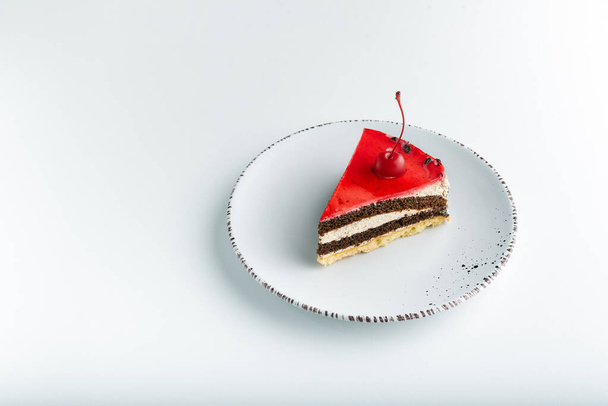 Sponge cake with red glaze and maraschino cherry on white plate - Foto, imagen