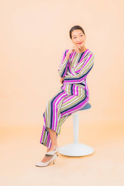 Portret mooie jonge aziatische vrouw zitten op stoel en glimlach met actie op kleur geïsoleerde achtergrond - Foto, afbeelding