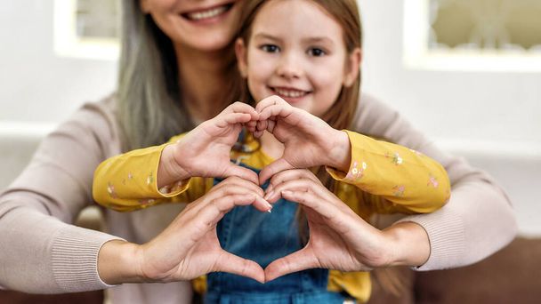 Spreading love. Close up portrait of little girl granddaughter spending time together with her loving granny. They are smiling and showing heart sign - Φωτογραφία, εικόνα