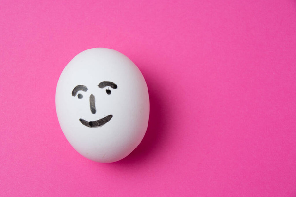 Egg with a happy face on a pink background with copy space - Fotó, kép