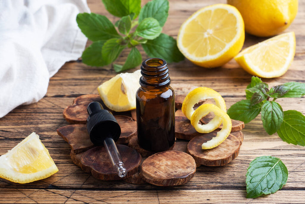 Lemon citrus fruit essential oil and mint, aromatherapy oil natural organic cosmetic on rustic wood background - 写真・画像