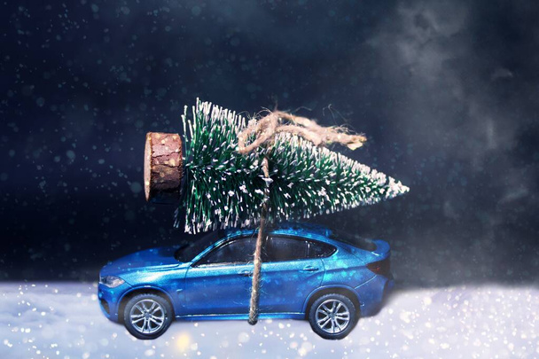 Голубой пассажирский автомобиль привязал рождественскую елку к крыше в тумане. Его snowy.Christmas концепция - автомобиль за рулем елки для красивой семьи Рождество. - Фото, изображение