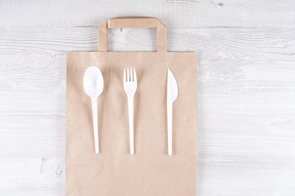 plastic fork, spoon, knife on paper bag. Eco-friendly food packaging and cotton eco bags on gray background with copy space. Carering of nature and recycling concept. containers for catering and - Foto, afbeelding