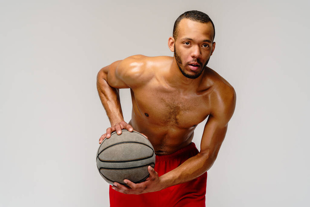Muscular african american sportsman playing basketball shitless over light grey background - Zdjęcie, obraz