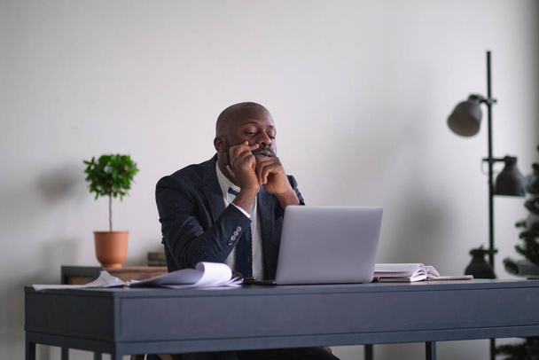 wütender junger afroamerikanischer Geschäftsmann. Unternehmer wütend und wütend mit einem Laptop in einem kleinen Büro oder Zuhause. - Foto, Bild