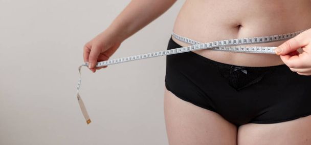 Woman measures her waist line. Woman wants to lose weight. Diet and healthy eating. Overweight women isolated - Fotó, kép