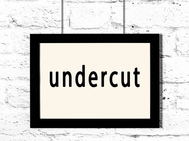 Μαύρο ξύλινο πλαίσιο με επιγραφή undercut κρέμεται σε λευκό τοίχο τούβλο  - Φωτογραφία, εικόνα