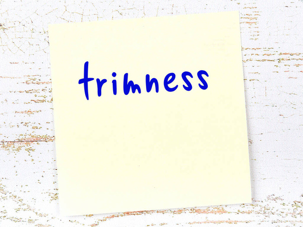 Yellow sticky note on wooden wall with handwritten inscription trimness - Foto, afbeelding