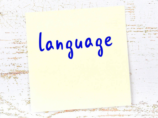 Έννοια της υπενθύμισης για τη γλώσσα. Κίτρινο κολλώδες φύλλο χαρτιού σε ξύλινο τοίχο με επιγραφή - Φωτογραφία, εικόνα