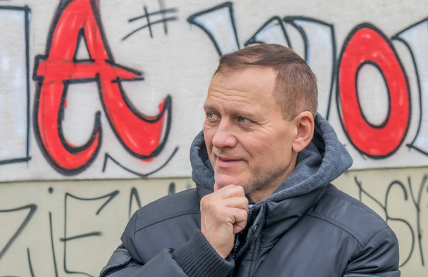 Egy 60 éves, aktív, jóképű, középkorú európai férfi áll egy festett fal mellett, és elgondolkodva mosolyog. - Fotó, kép