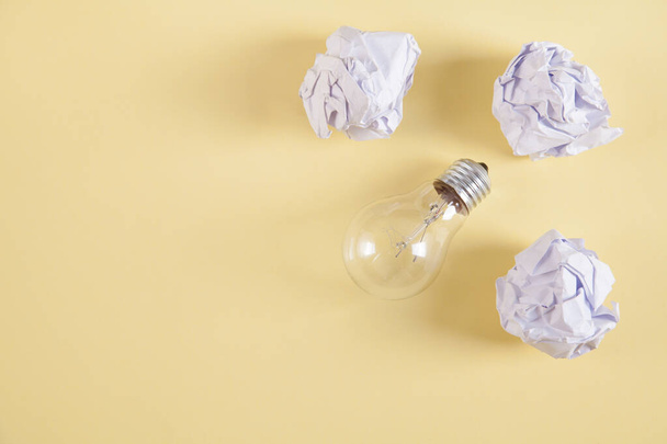 Creativity inspiration. Light bulb and crumpled paper balls on yellow background. - Photo, Image