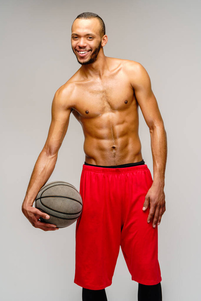 Muscular african american sportsman playing basketball shitless over light grey background - Fotó, kép