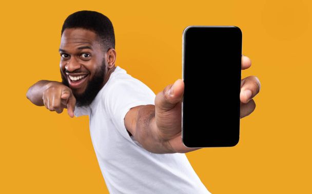 Ενθουσιασμένος μαύρος που παρουσιάζει την κενή οθόνη Smartphone πέρα από το κίτρινο υπόβαθρο - Φωτογραφία, εικόνα