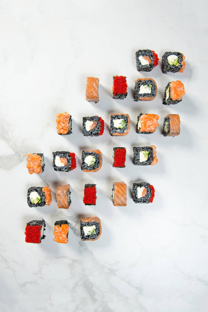 Top view of black rice Japanese sushi roll pieces served on white marble background. Sushi with salmon, avocado, cream cheese and red flying fish roe Tobiko (Masago). Large set of seafood sushi rolls - Photo, Image