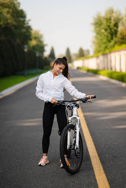 Красива дівчина позує на білому велосипеді. Прогулянка на природі
. - Фото, зображення