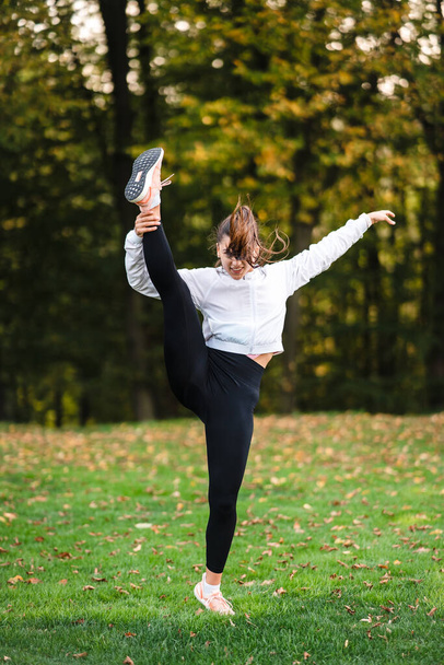 Γυναίκα στο αθλητικό ντύσιμο στο πάρκο κάνει split στέκεται. - Φωτογραφία, εικόνα