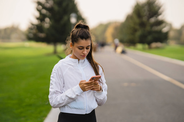 Girl athlete holds and uses smartphone after jogging. - Φωτογραφία, εικόνα