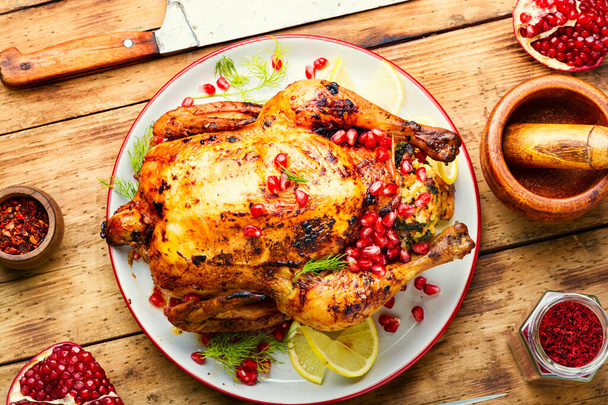 Ολόκληρο κοτόπουλο ψημένο με μούρα ροδιού σε πιάτο σε ξύλινο ρουστίκ φόντο. - Φωτογραφία, εικόνα