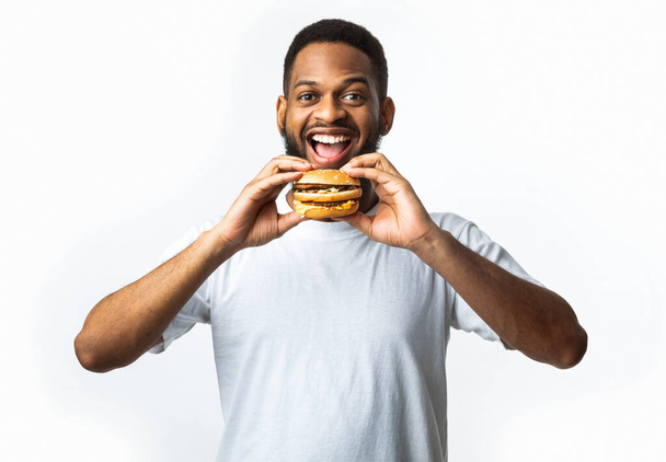 Africano chico mordiendo hamburguesa comer comida chatarra poco saludable, fondo blanco - Foto, imagen