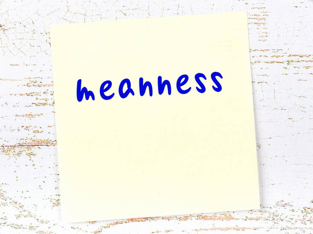Concept of reminder about meanness. Yellow sticky sheet of paper on wooden wall with inscription - Photo, Image