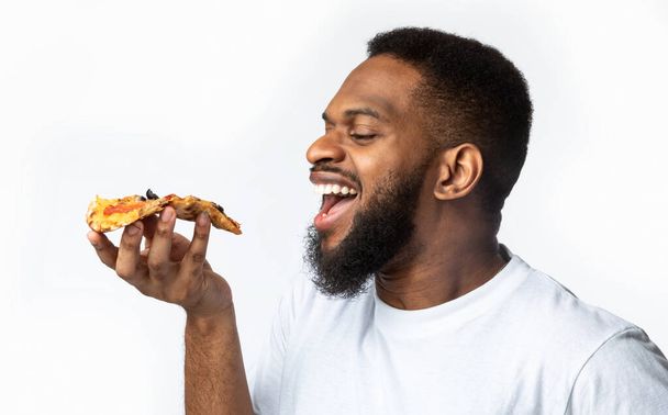 Africano comiendo rebanada de pizza, fondo blanco, vista lateral - Foto, Imagen