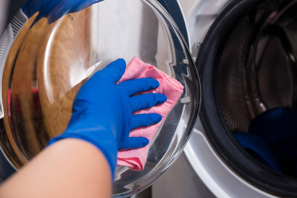 Una mano in guanti lava le porte della lavatrice con uno straccio. - Foto, immagini
