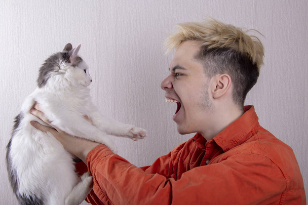 Un adolescente sostiene a un gato en sus brazos y le grita. - Foto, Imagen