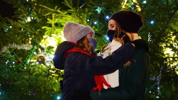 Mutter und Tochter in Schutzmasken am Weihnachtsbaum. - Foto, Bild